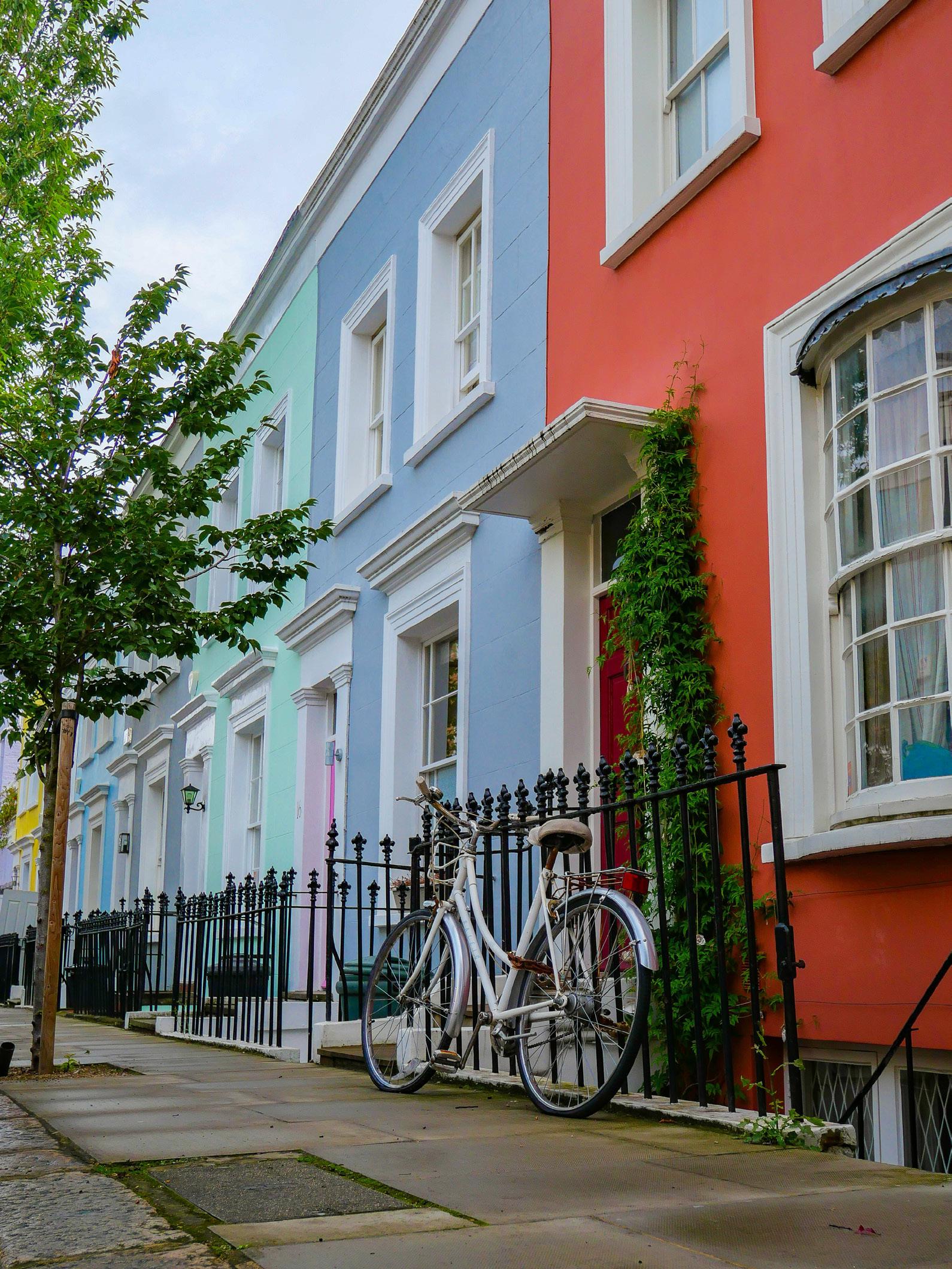 A row of brightly colored townhouses in London, a quintessential sight. A white bicycle is parked in front of one of the houses, adding to the charm of the scene. This is a typical example of the properties managed by Beacons Way Property Management.