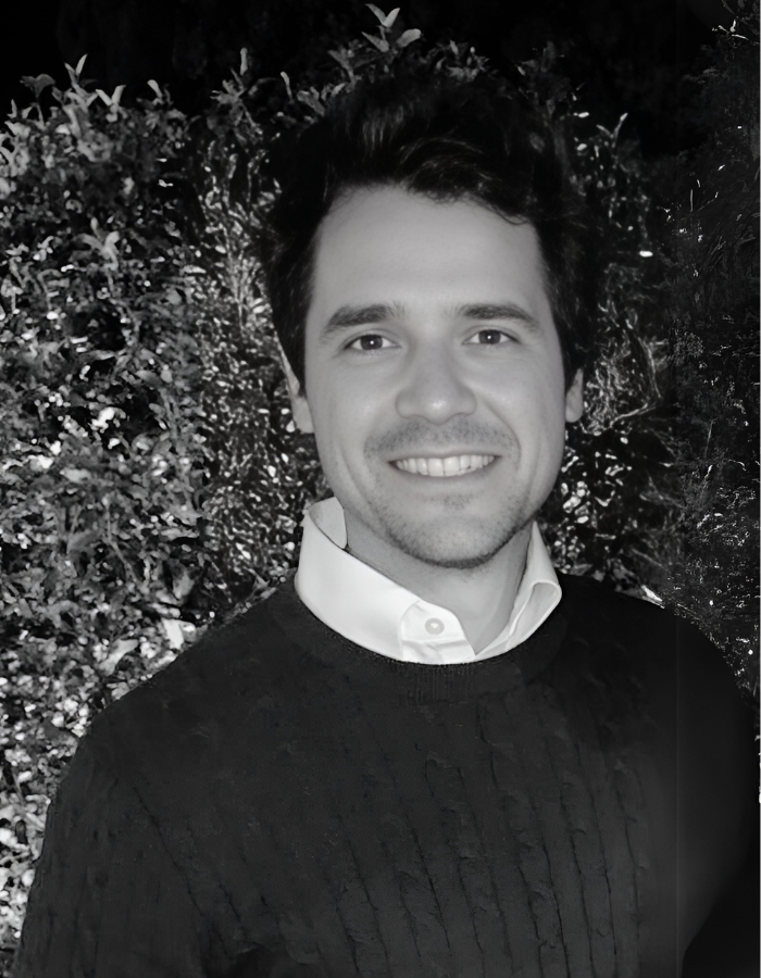 A headshot of Hugo, one of the co-founders of Beacons Way Property Management, in front of a leafy background. He is smiling and wearing a sweater over a collared shirt.