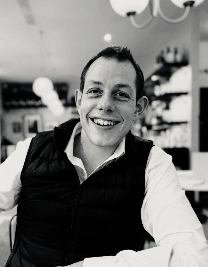 A headshot of Sam, a member of the Beacons Way Property Management team. He is smiling and wearing a vest over a collared shirt.